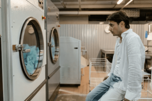 A man sits near commercial dryers, reflecting on choosing between gas and electric dryers for his business.