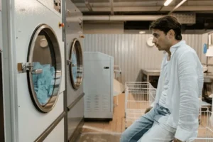 A man sits near commercial dryers, reflecting on choosing between gas and electric dryers for his business.