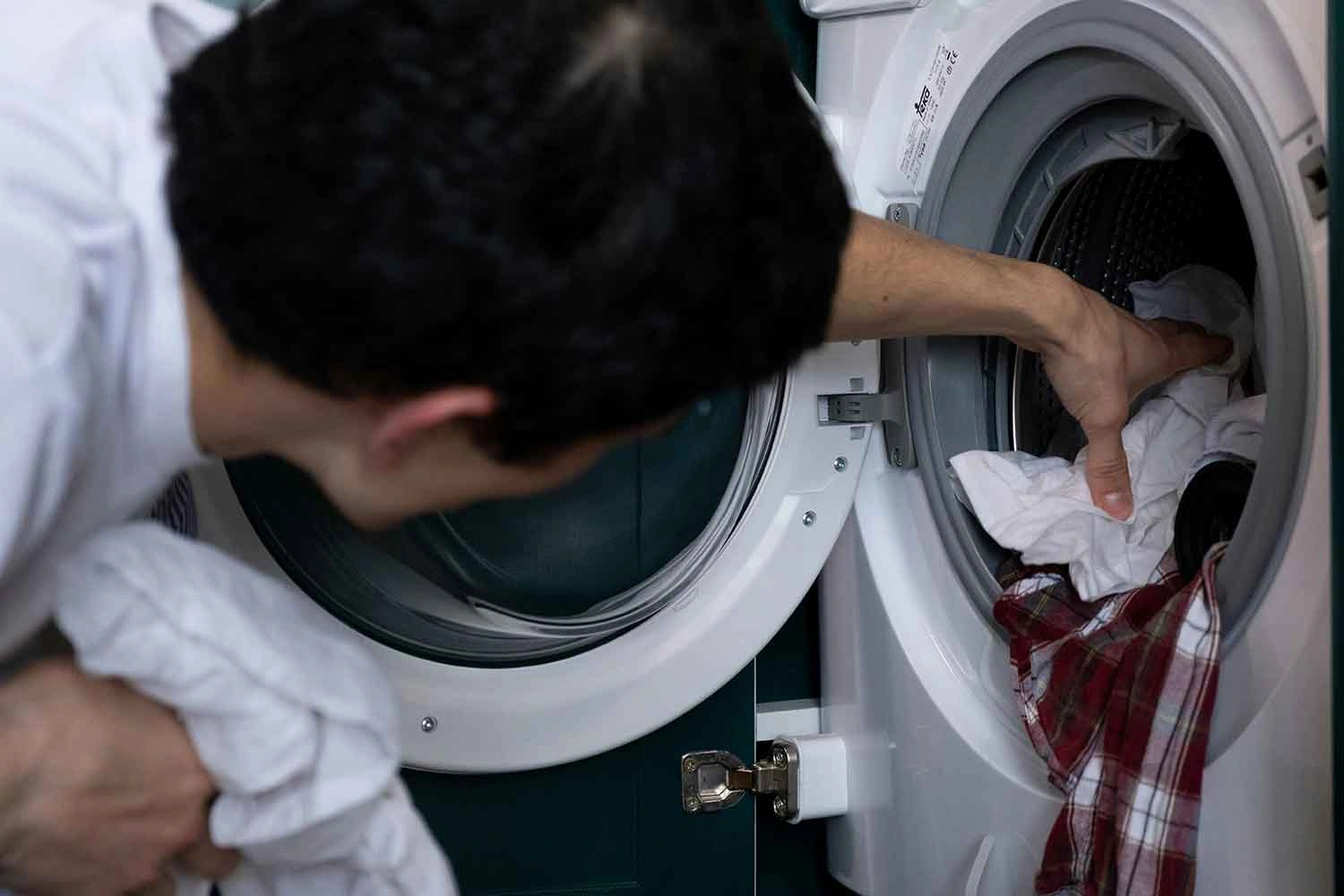 Man loading laundry into a washing machine, highlighting common laundry mistakes like overloading or mixing fabrics. Learn proper washing techniques!