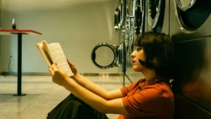 A student reads a book while waiting for laundry to finish, making the most of downtime in a clean, modern campus laundry room.