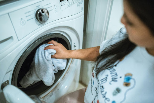 Resident loading laundry into a front-load washer, highlighting the need for well-maintained, easy-to-use machines in apartment laundry rooms.