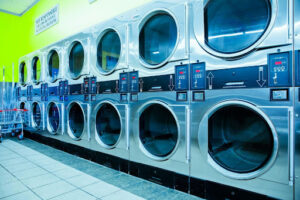 Row of industrial stainless steel dryers in a commercial laundromat, illustrating high-capacity smart laundry equipment for faster turnaround.