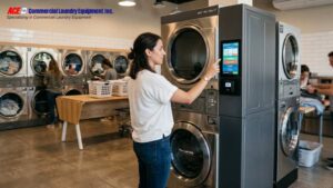 Resident operating a stacked commercial washer and dryer in a clean self-service laundry room.