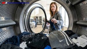 Person loading athletic clothes and towels into a commercial laundry machine at a laundromat.